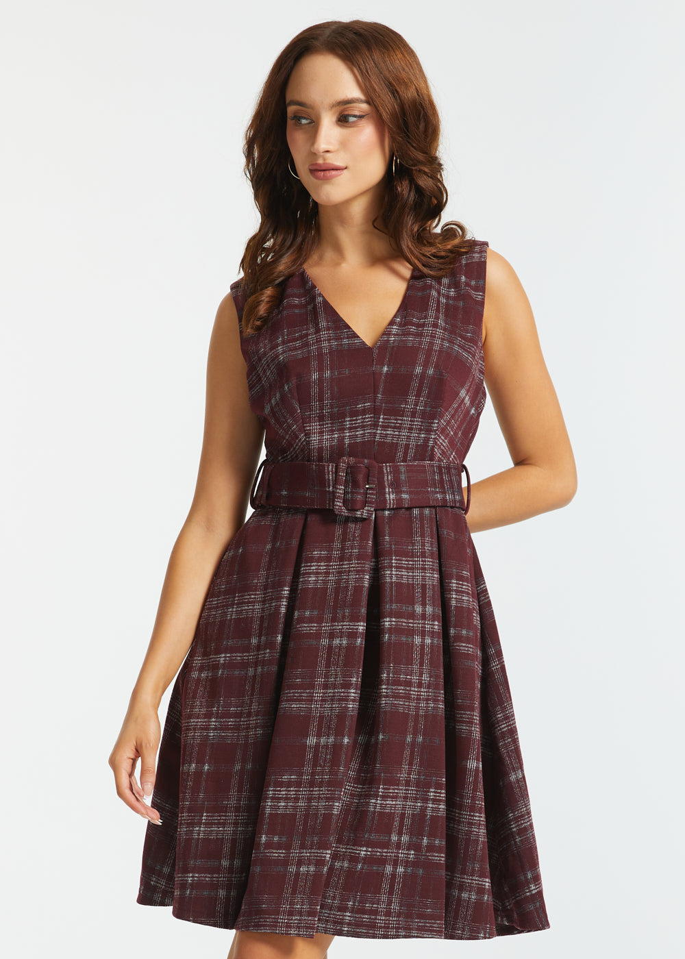 A woman modeling a sleeveless V-neck plaid dress with a matching waist belt, shown against a plain light gray studio background.
