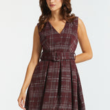 A woman modeling a sleeveless V-neck plaid dress with a matching waist belt, shown against a plain light gray studio background.
