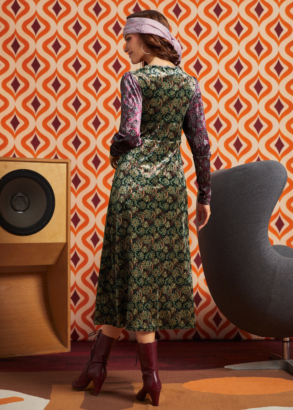 Woman wearing green and burgundy mixed paisley midi dress with burgundy boots, full back view