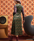 Woman wearing green and burgundy mixed paisley midi dress with burgundy boots, full back view