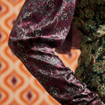 Close-up of burgundy paisley long sleeve and cuff beside contrasting green paisley bodice