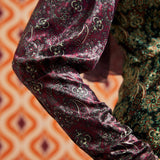 Close-up of burgundy paisley long sleeve and cuff beside contrasting green paisley bodice