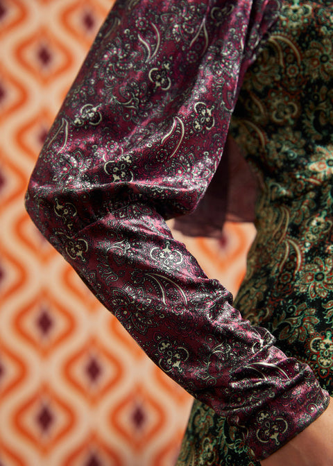 Close-up of burgundy paisley long sleeve and cuff beside contrasting green paisley bodice