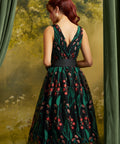 Back view of the floral embroidered midi dress showing the V-back neckline, fitted waist, black sash, and flowing skirt.