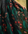 Close-up of the sheer black mesh skirt with embroidered emerald-green leaves, coral-red flowers, and delicate floral stems.