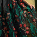 Close-up of the sheer black mesh skirt with embroidered emerald-green leaves, coral-red flowers, and delicate floral stems.