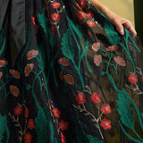 Close-up of the sheer black mesh skirt with embroidered emerald-green leaves, coral-red flowers, and delicate floral stems.