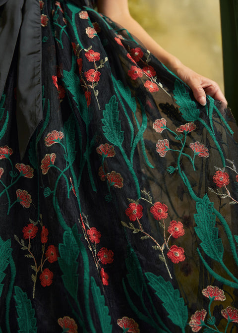 Close-up of the sheer black mesh skirt with embroidered emerald-green leaves, coral-red flowers, and delicate floral stems.
