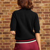 Back view of the black cotton Hattie Half-Sleeve Sweater showing the plain knit back, ribbed short sleeve cuffs, and contrasting burgundy, black, and cream striped hem.