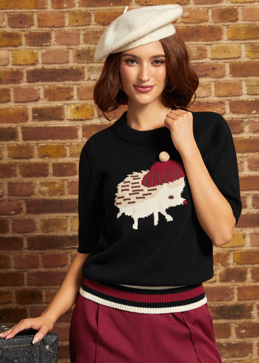 Model wearing the black ModCloth Hattie Half-Sleeve Sweater featuring a cream hedgehog in a burgundy beret with a pom-pom, striped ribbed hem, and elbow-length sleeves, styled with burgundy trousers and a cream beret.