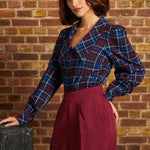 Model wearing a vintage-inspired burgundy and blue plaid blouse tucked into high-waisted burgundy trousers, showing its dramatic collar and softly puffed long sleeves.