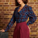 Model wearing a vintage-inspired burgundy and blue plaid blouse tucked into high-waisted burgundy trousers, showing its dramatic collar and softly puffed long sleeves.