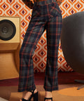 Woman wearing dark navy plaid high-waisted pants with rust and olive accents, brown cat cardigan, and black platform heels, front view