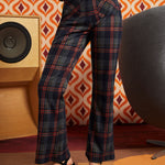 Woman wearing dark navy plaid high-waisted pants with rust and olive accents, brown cat cardigan, and black platform heels, front view