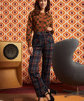 A woman models a two-piece outfit consisting of a brown long-sleeve top with a black cat pattern and dark plaid trousers.
