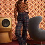 A woman models a two-piece outfit consisting of a brown long-sleeve top with a black cat pattern and dark plaid trousers.