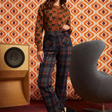 A woman models a two-piece outfit consisting of a brown long-sleeve top with a black cat pattern and dark plaid trousers.