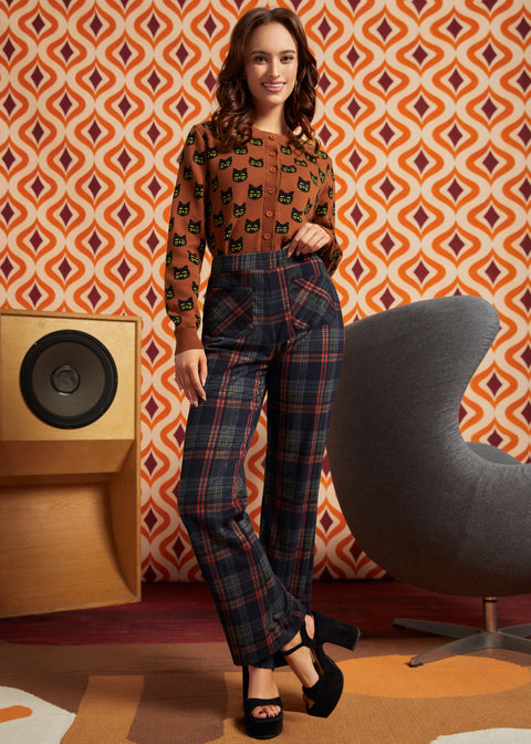 A woman models a two-piece outfit consisting of a brown long-sleeve top with a black cat pattern and dark plaid trousers.