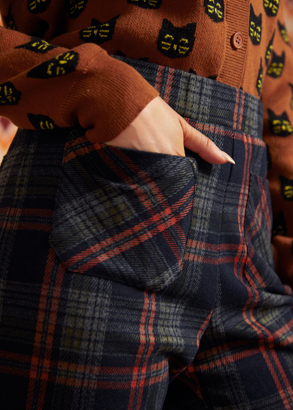 Close-up of dark plaid pants showing front patch pocket, high waistband, and rust and olive plaid pattern