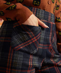 Close-up of dark plaid pants showing front patch pocket, high waistband, and rust and olive plaid pattern