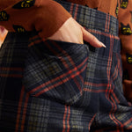 Close-up of dark plaid pants showing front patch pocket, high waistband, and rust and olive plaid pattern