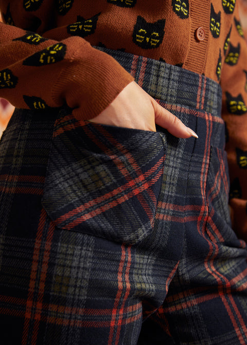 Close-up of dark plaid pants showing front patch pocket, high waistband, and rust and olive plaid pattern