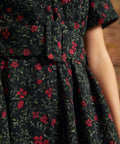 Close-up of the matching fabric belt with covered buckle, button-front waist, and gathered skirt on a black and red floral corduroy dress.