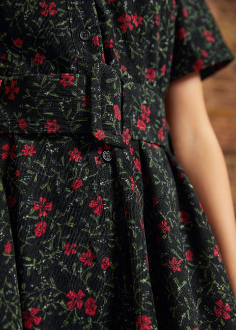Close-up of the matching fabric belt with covered buckle, button-front waist, and gathered skirt on a black and red floral corduroy dress.