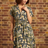 Model wearing a vintage-inspired navy squirrel and floral print button-front midi dress with short sleeves, contrast piping, and a tied waist belt.