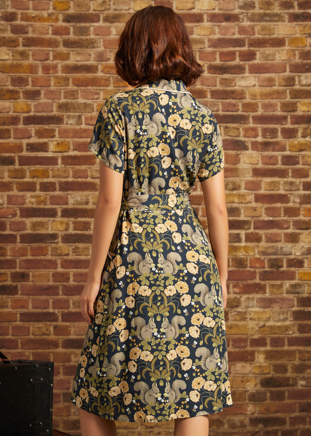 Back view of a short-sleeve navy woodland print midi dress featuring squirrels, golden flowers, a notched collar, and a matching fabric waist tie.