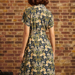 Back view of a short-sleeve navy woodland print midi dress featuring squirrels, golden flowers, a notched collar, and a matching fabric waist tie.