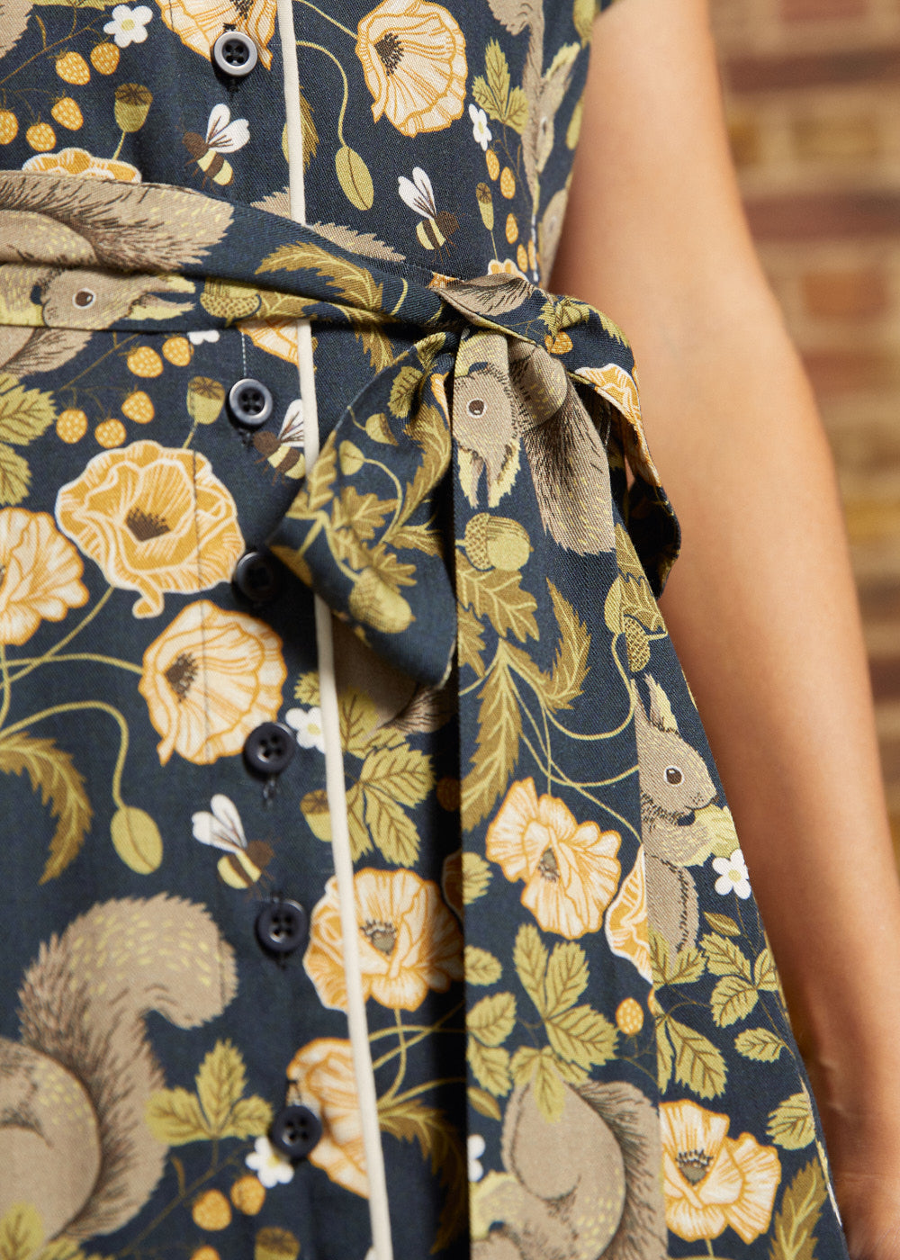 Close-up of the removable fabric waist belt tied in a bow on a navy squirrel and botanical print dress with functional black buttons.
