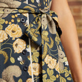 Close-up of the removable fabric waist belt tied in a bow on a navy squirrel and botanical print dress with functional black buttons.
