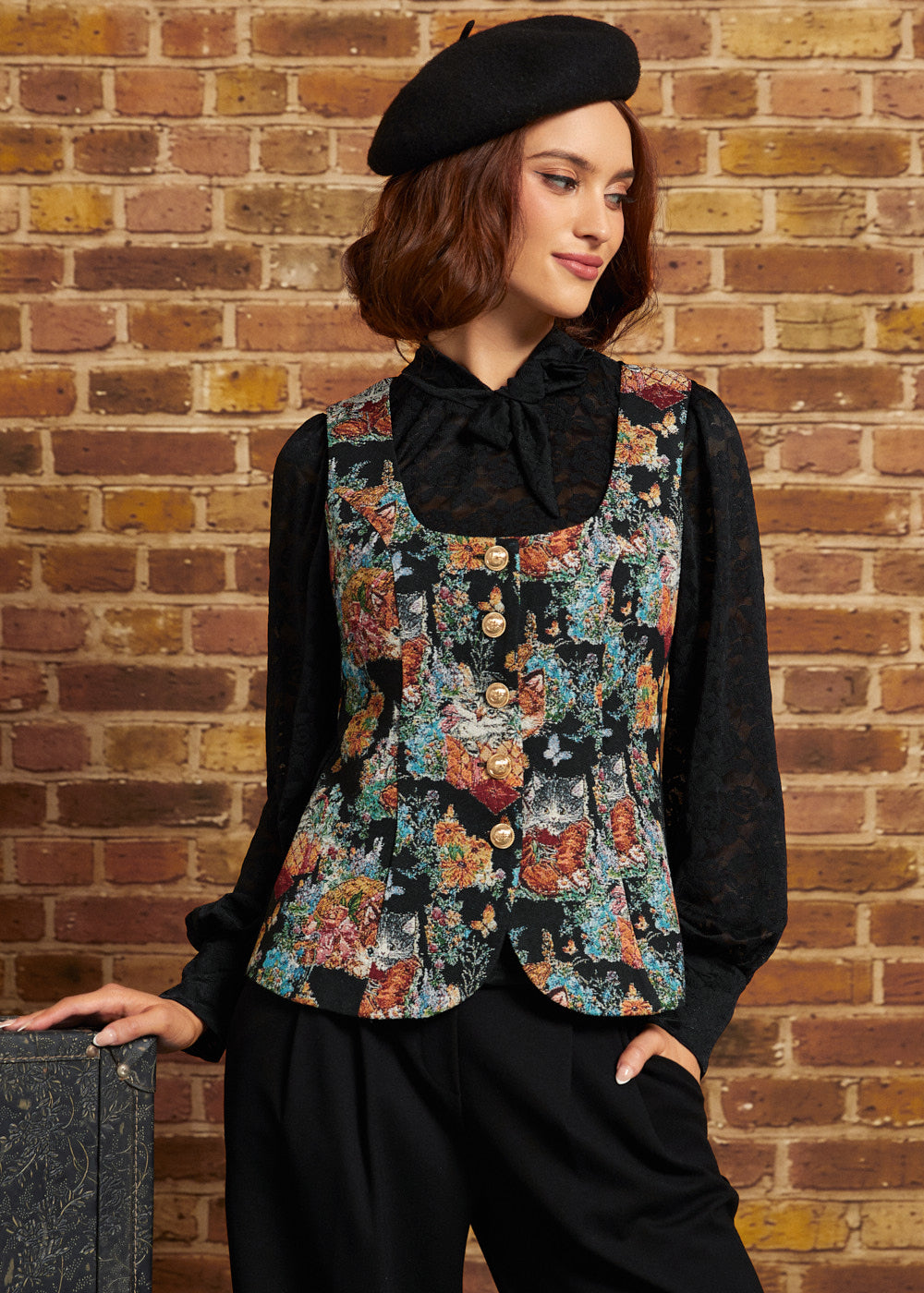 Model wearing the Winifred Waistcoat Vest in Tapestry Tabbies with a black lace bow blouse, black trousers, and beret, showing the tailored cat tapestry design and gold buttons.