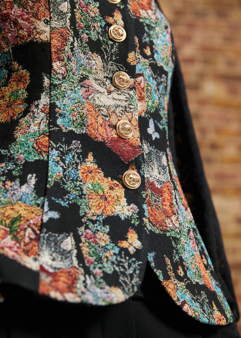 Close-up of a ModCloth vintage-inspired cat and floral tapestry vest showing ornate gold-tone buttons, tailored seams, and subtly flared front hem.
