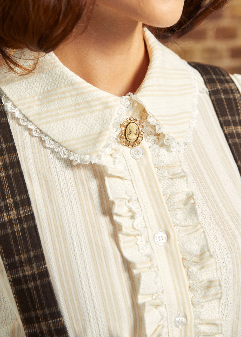 Close-up of the lace-trimmed collar, decorative cameo-style accent, textured fabric, and ruffled button placket on an ivory Victorian blouse.
