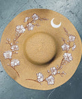 Straw hat with floral designs and a moon on a gray surface