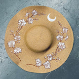 Straw hat with floral designs and a moon on a gray surface