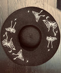 Black sun hat with white butterfly designs on a wooden surface