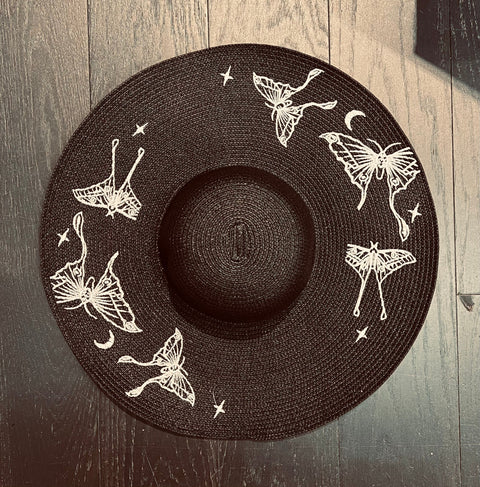 Black sun hat with white butterfly designs on a wooden surface