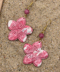 Pink flower-shaped earrings with gold hooks on a sandy surface