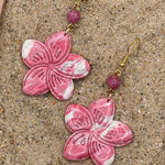 Pink flower-shaped earrings with gold hooks on a sandy surface