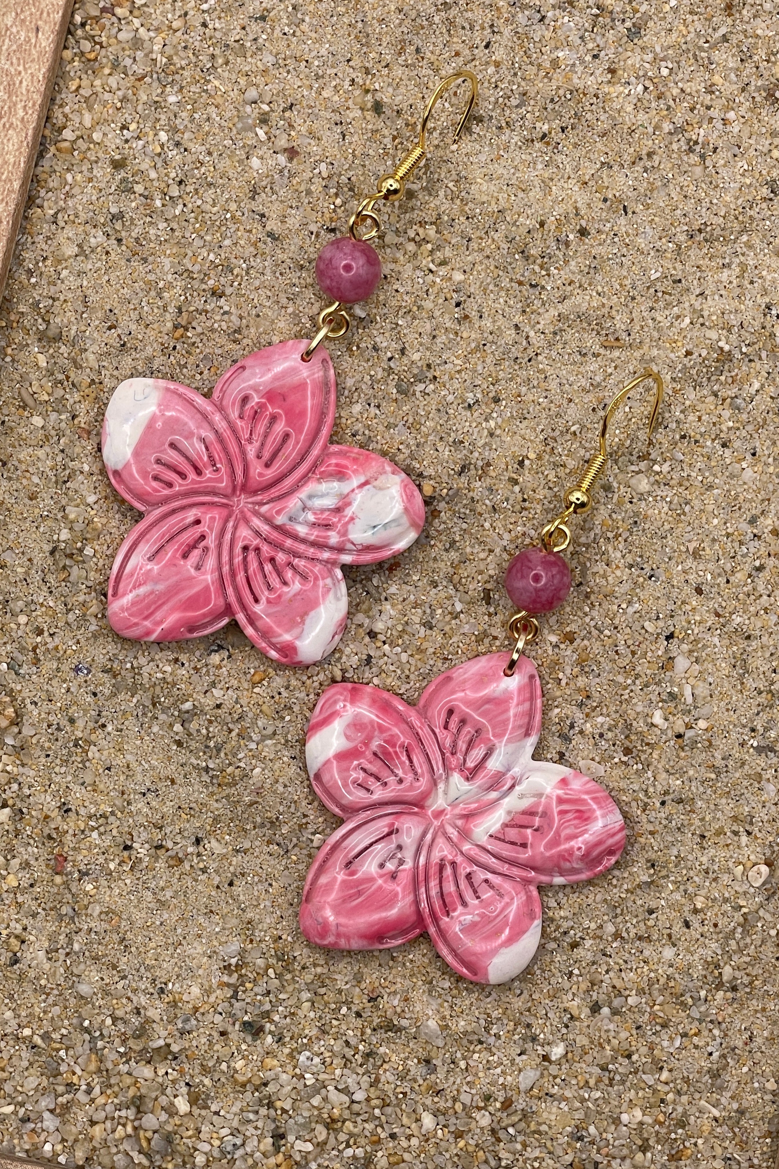 Pink flower-shaped earrings with gold hooks on a sandy surface