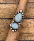 Silver ring with two light blue gemstones on a wooden stick
