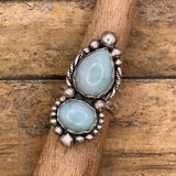 Silver ring with two light blue gemstones on a wooden stick