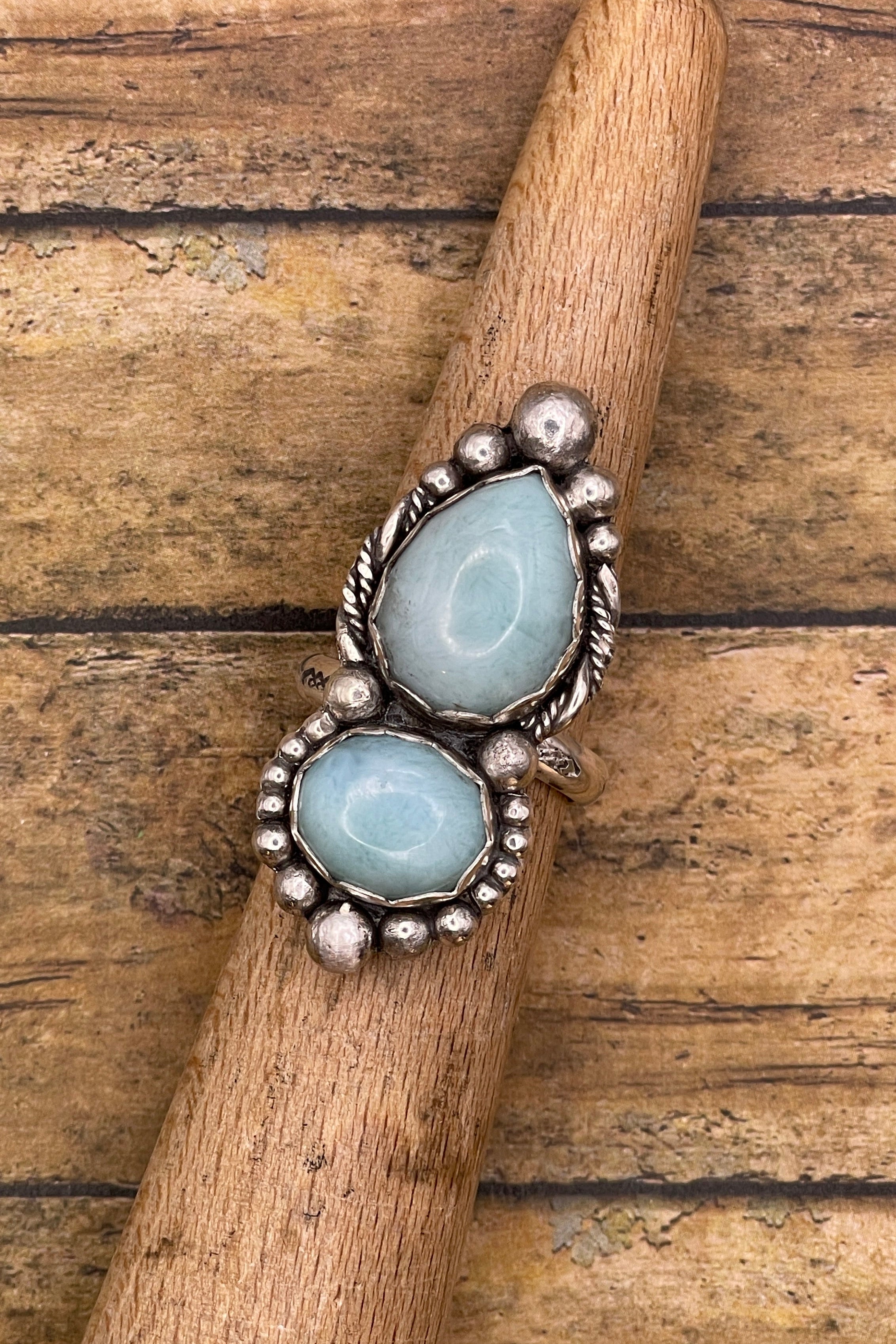 Silver ring with two light blue gemstones on a wooden stick