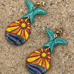 Colorful mermaid tail earrings on a sandy surface