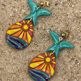 Colorful mermaid tail earrings on a sandy surface