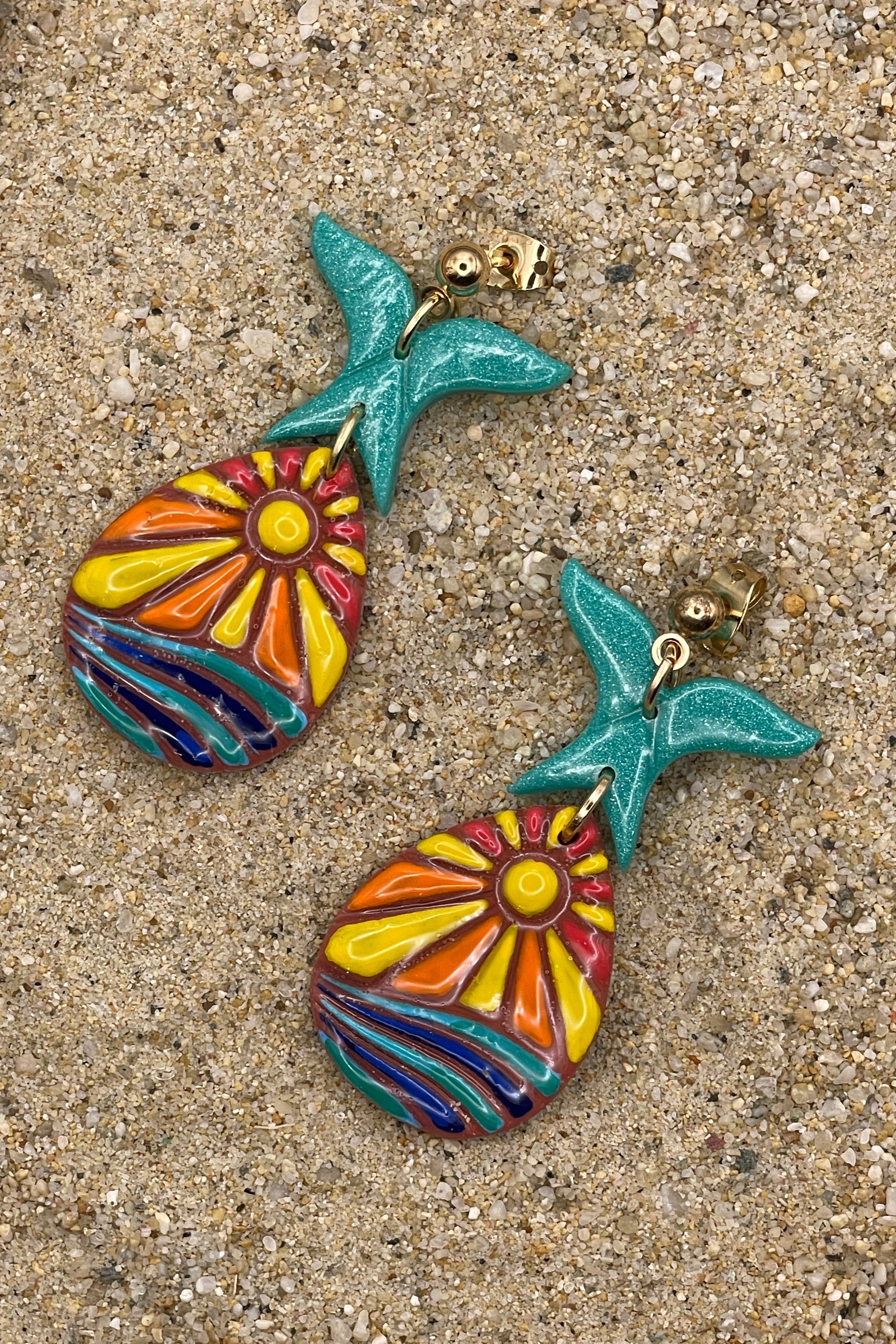 Colorful mermaid tail earrings on a sandy surface
