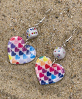Heart-shaped earrings with colorful heart pattern on a sandy surface